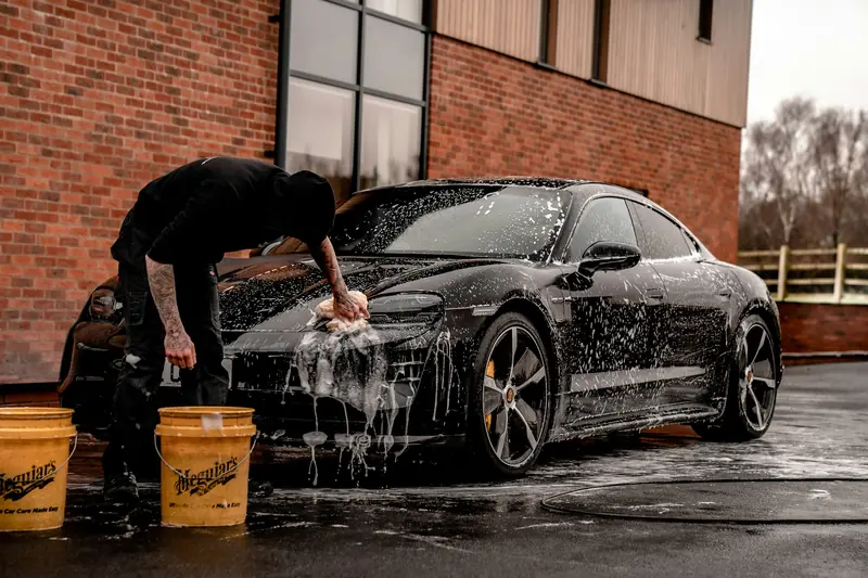 Detailer hand washing a black car with foam and buckets